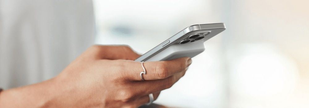 Hand håller en silverfärgad smartphone, relevant vid köp av rekonditionerad mobil
